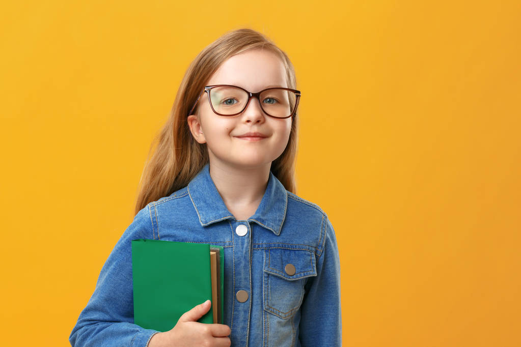 Piccola studentessa in camicia di jeans su sfondo giallo. Un bambino con gli occhiali tiene un libro. Il concetto di istruzione e scuola
. - Foto, immagini