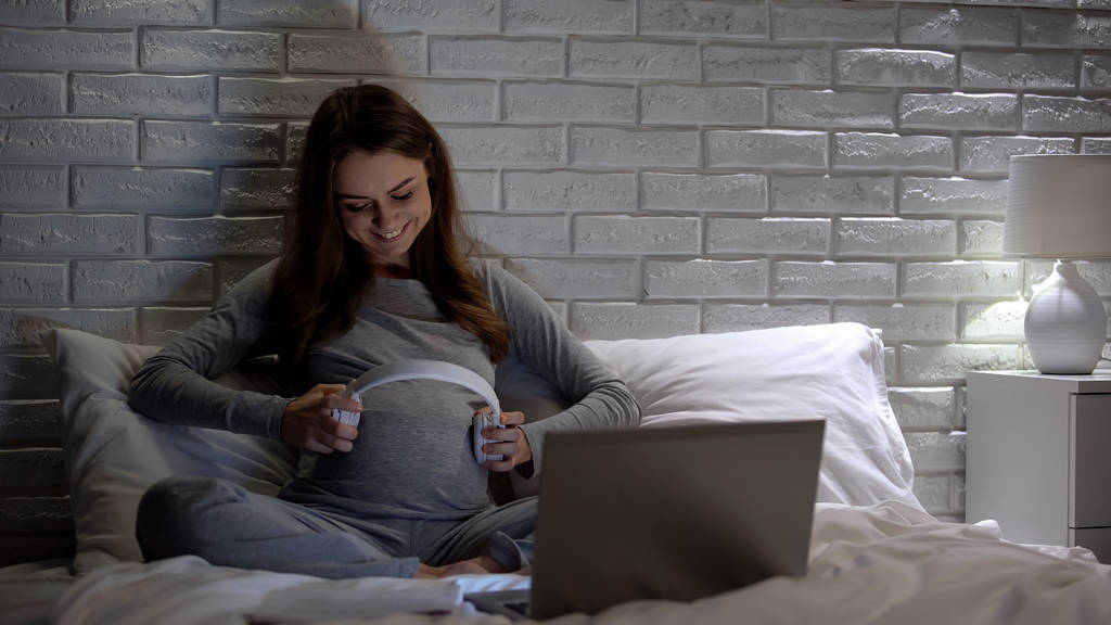 Iloinen raskaana oleva nainen laittaa kuulokkeet vatsaan, rentouttavaa musiikkia vauvalle
 - Valokuva, kuva