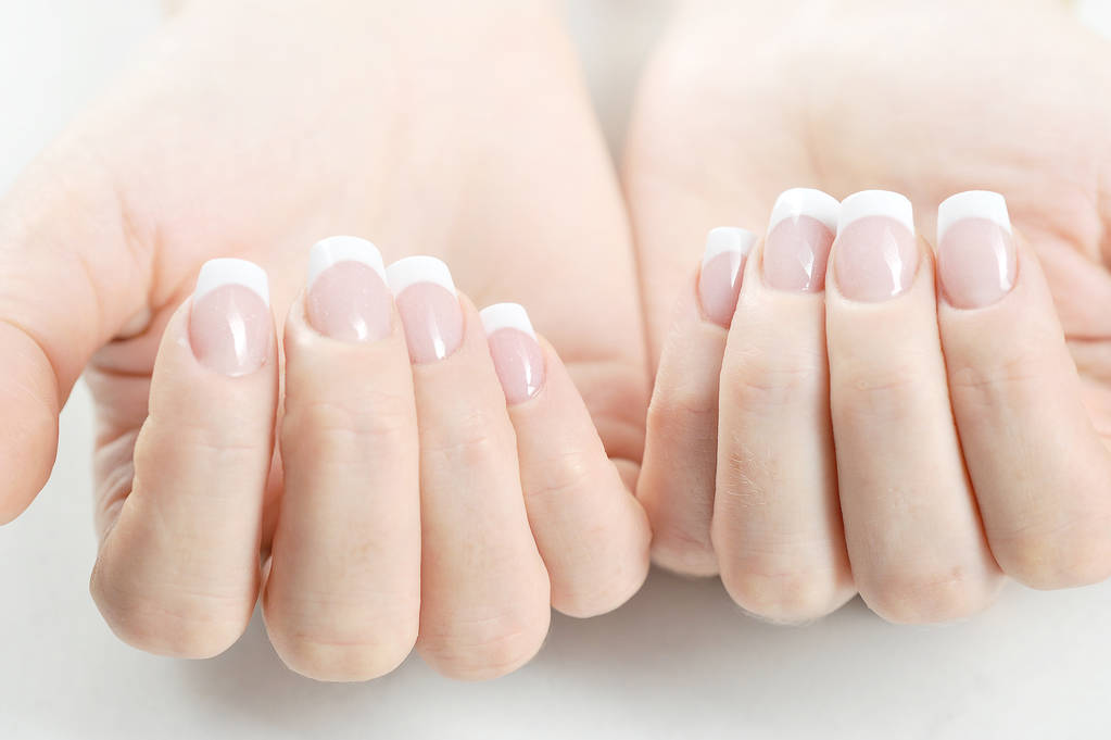 Twee vrouwenhanden met French manicure. Close-up. Witte achtergrond. - Foto, afbeelding