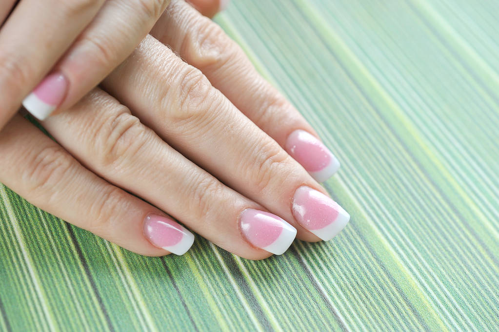Franse manicure op vrouwelijke hand close-up. Groene achtergrond. Vrije ruimte om tekst te plaatsen. - Foto, afbeelding