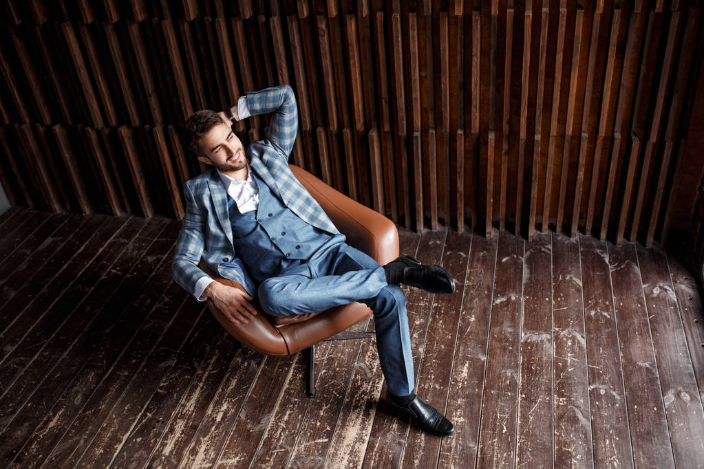 Jóvenes hombres de negocios exitosos con un traje azul en una jaula están sentados en una silla de cuero. joven con barba sonriendo. - Foto, Imagen