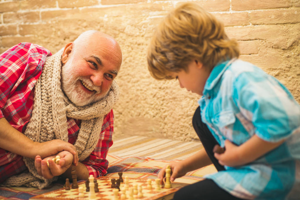 Ανώτερος άνθρωπος σκέφτεται την επόμενη κίνησή του σε ένα παιχνίδι σκάκι. Τσέσμαν. Ώριμος άντρας με μικρό αγόρι να παίζει σκάκι. Ρουά ματ. Γενιές. - Φωτογραφία, εικόνα