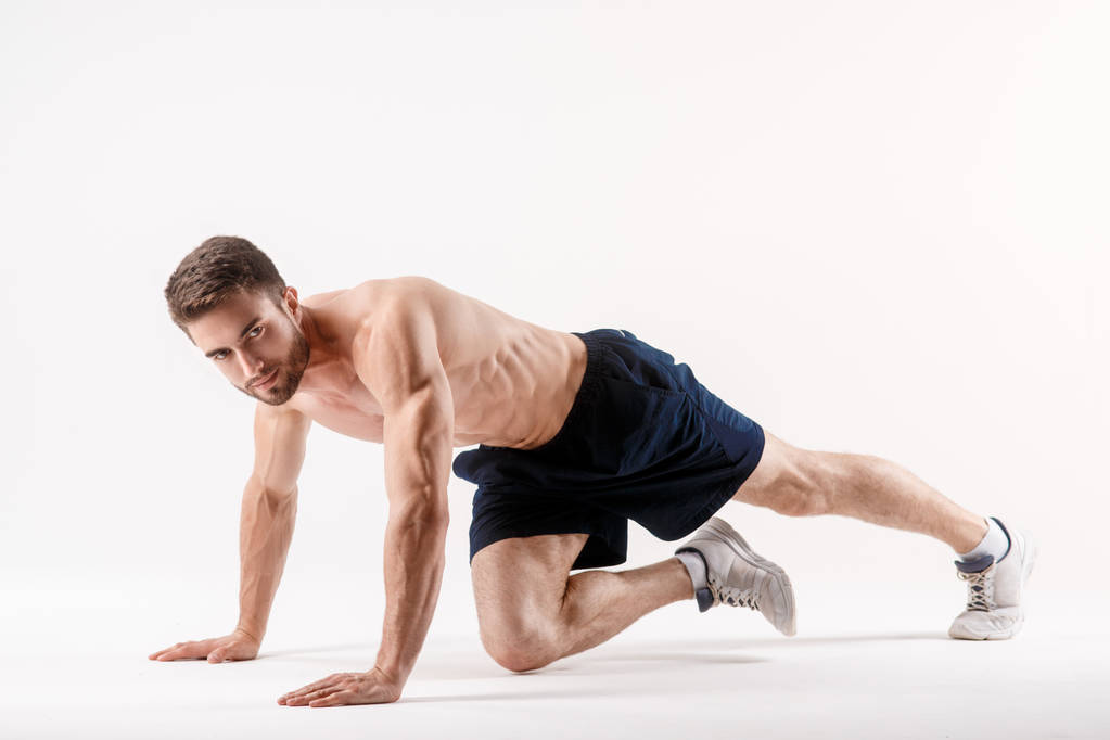 молодой человек с бородой спортивного телосложения делает упражнение на мышцы брюшной полости на белом изолированном фоне, спортсмен занимается спортом, упражняется на мышцах пресса - Фото, изображение