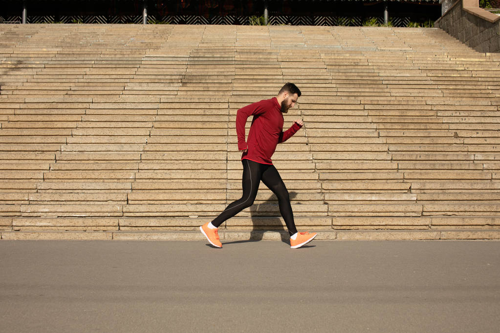 Молодой бородатый мужчина в спортивной одежде бежит по лестнице
 - Фото, изображение