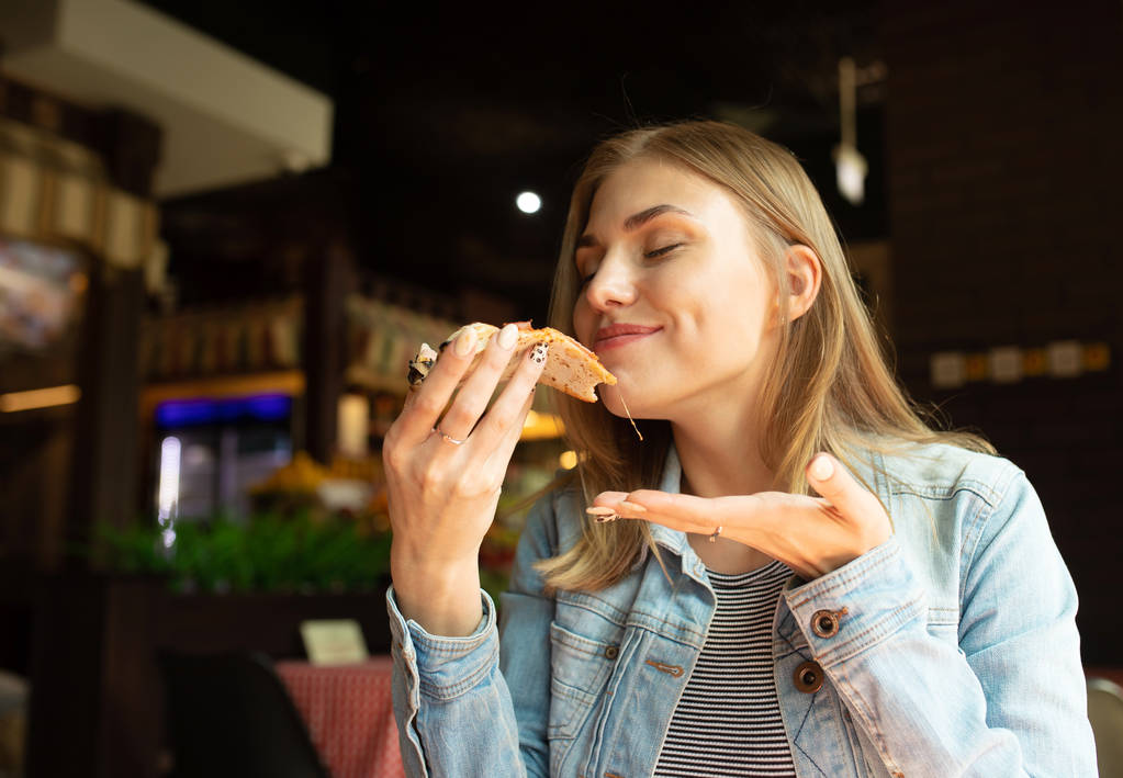 Retrato de mujer rubia comiendo pizza recién horneada en la cafetería
 - Foto, imagen