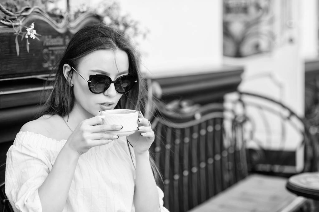 Girl enjoy morning coffee. Woman in sunglasses drink coffee outdoors. Girl relax in cafe cappuccino cup. Caffeine dose. Coffee for energetic successful day. Waiting for date. Breakfast time in cafe - Photo, Image