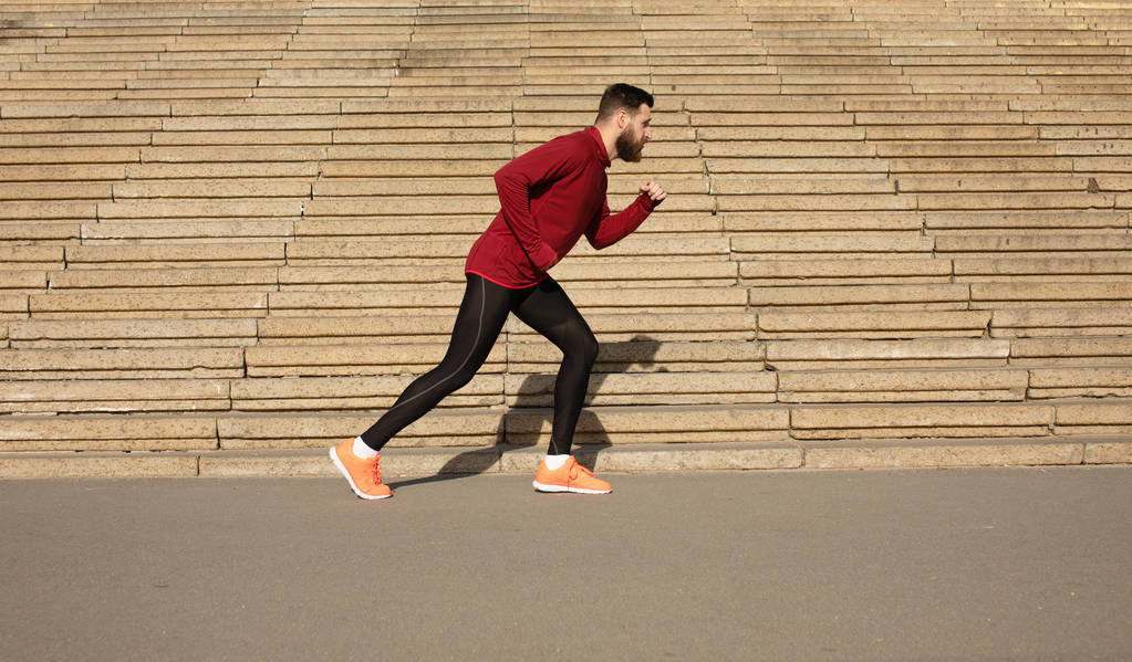 Giovane uomo barbuto in abbigliamento sportivo correre su sfondo scale
 - Foto, immagini