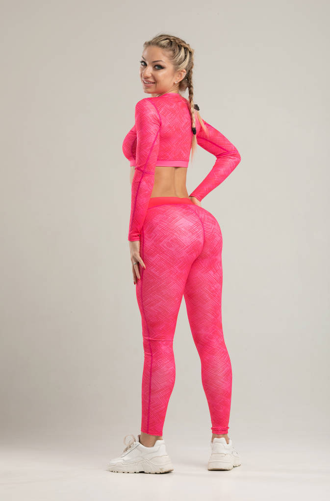 Jonge blonde fit vrouw in helder roze Sportswear poseren in Studio - Foto, afbeelding