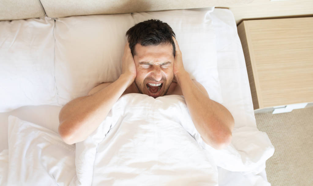 Dühös ember, amely fül szóló az ágyban kora reggel - Fotó, kép