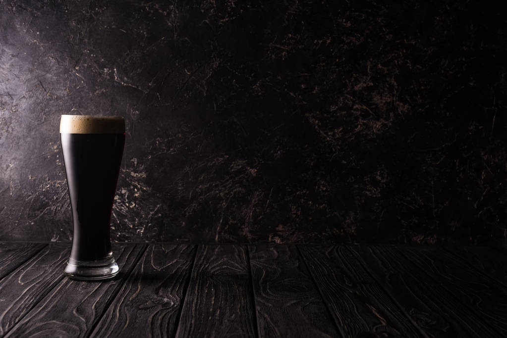 glas donker bier op houten tafel met schaduw - Foto, afbeelding