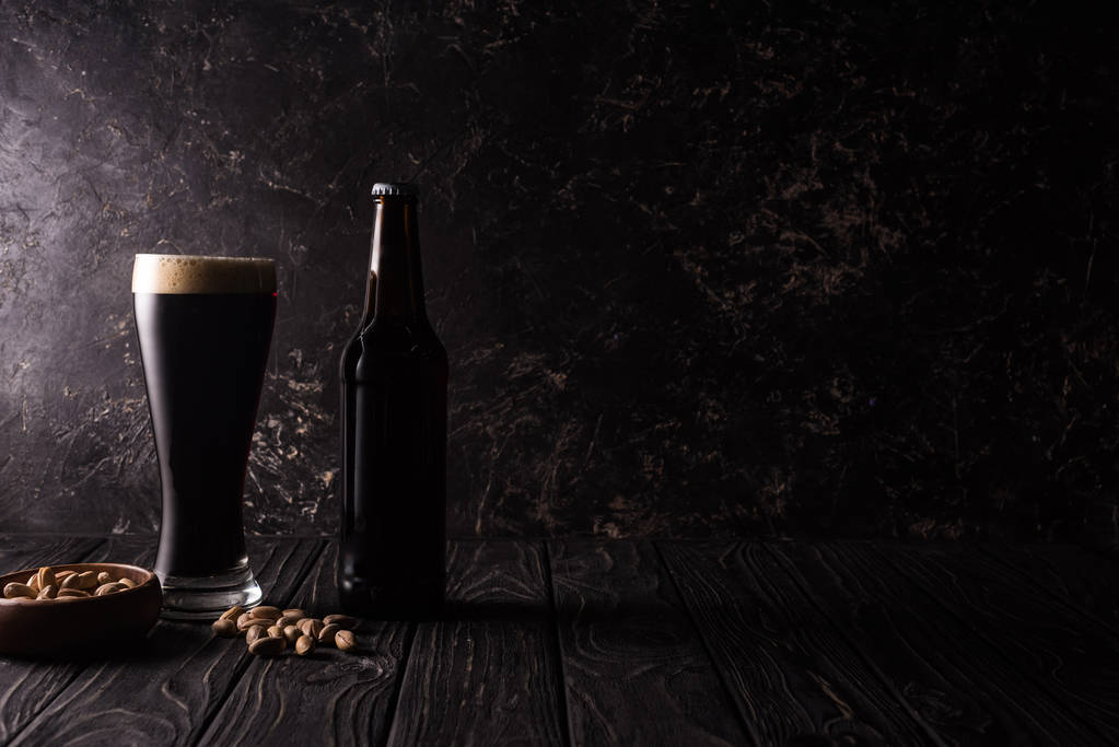 ποτήρι και μπουκάλι μπύρας κοντά σε μπολ με φιστίκια σε ξύλινο τραπέζι - Φωτογραφία, εικόνα
