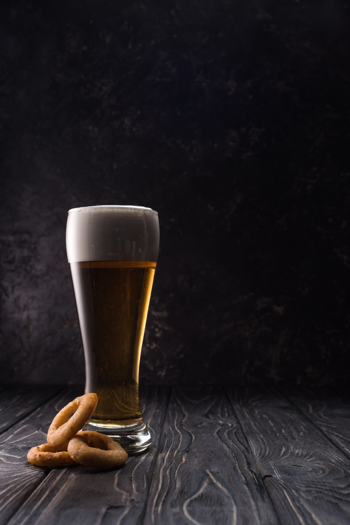 vaso de cerveza fresca y ligera cerca de aros de cebolla frita en mesa de madera
 - Foto, imagen