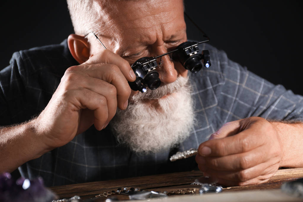 Мужчина ювелир оценивает бриллиантовую брошь в мастерской, вид крупным планом
 - Фото, изображение