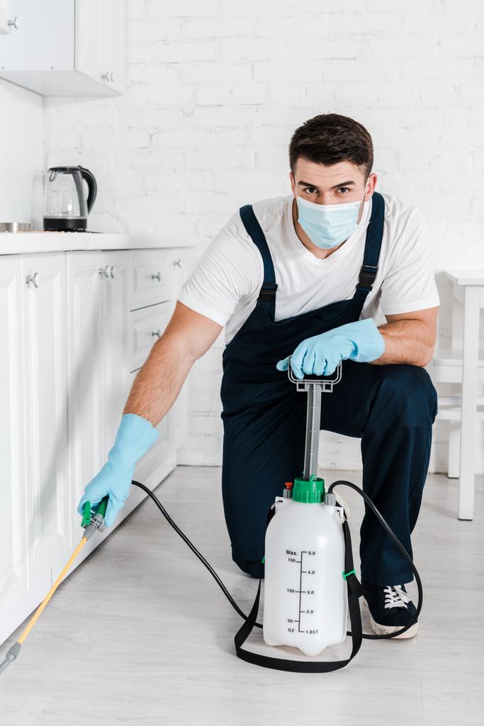 exterminator in uniform holding toxic spray near kitchen cabinet  - Photo, Image