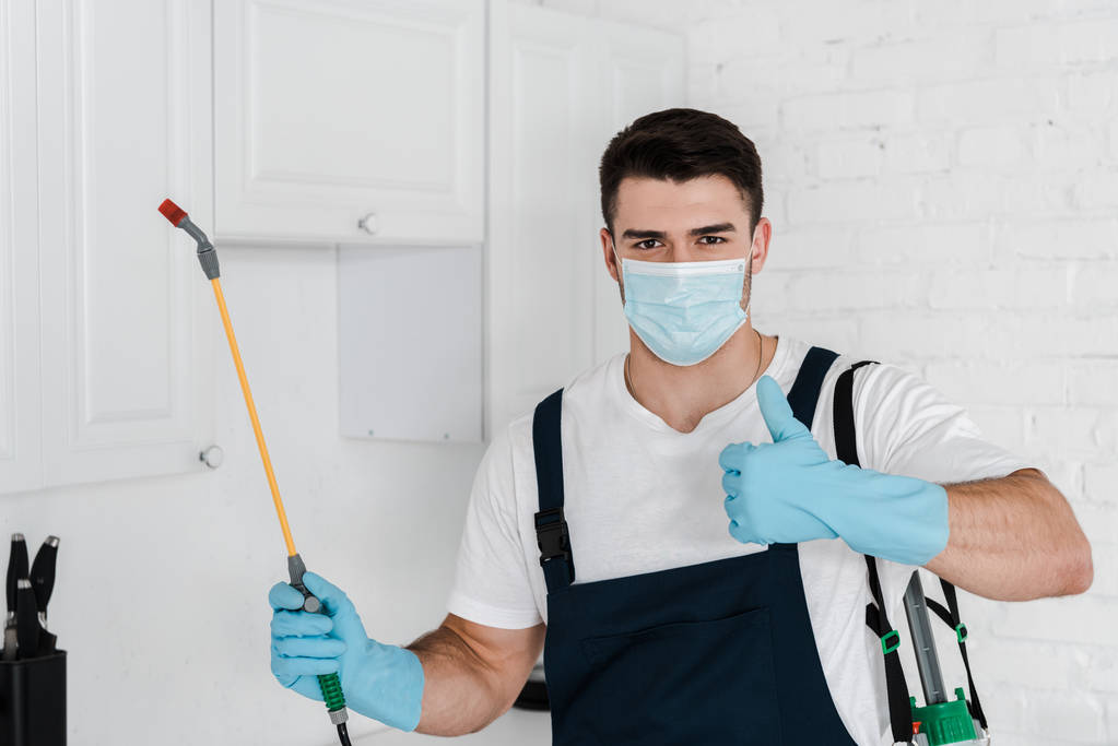 exterminator in uniform holding toxic spray and showing thumb up - Photo, Image