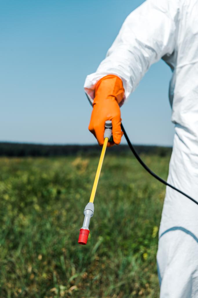 cropped view of exterminator in orange latex glove and white uniform holding spray outside  - Photo, Image