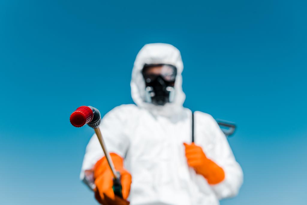 selectieve focus van Exterminator skin in wit uniform en latex handschoenen houden spray buiten  - Foto, afbeelding
