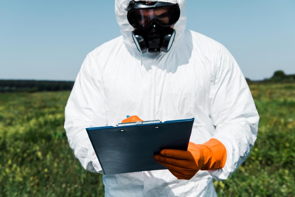 man in protective mask and uniform writing while holding clipboard  - Photo, Image