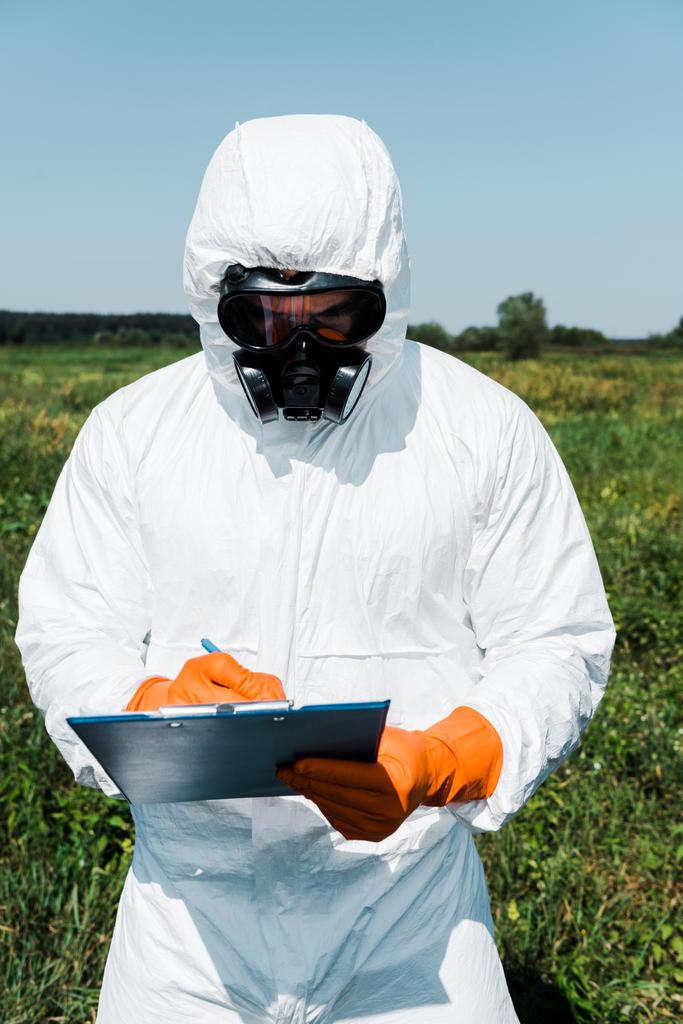 Exterminator skin in beschermend masker en uniform schrijven terwijl het Klembord vasthoudt  - Foto, afbeelding