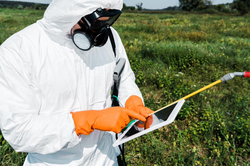 exterminator in protective mask and uniform pointing with finger at laptop - Photo, Image