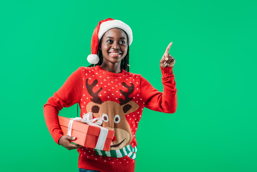 Afrikkalainen amerikkalainen nainen joulun villapaita ja Santa hattu tilalla läsnä ja sormella eristetty vihreä
 - Valokuva, kuva