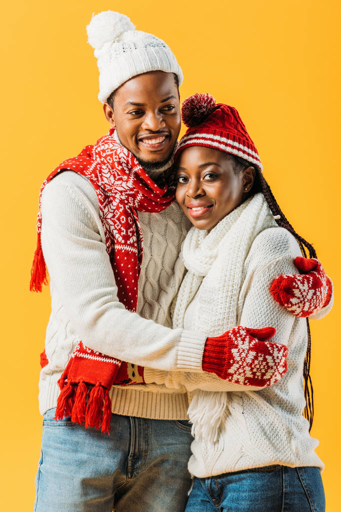 Couple afro-américain en tenue d'hiver confortable regardant la caméra et s'embrassant isolés sur jaune
 - Photo, image