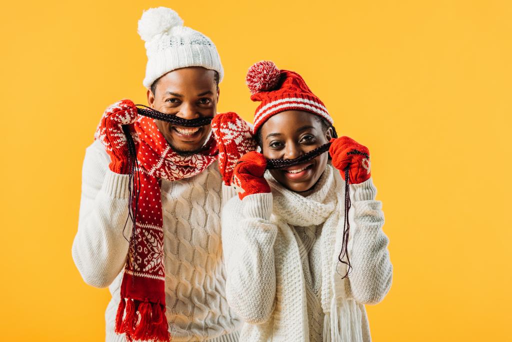 Afrikanisch-amerikanisches Paar im Winteroutfit, Schnurrbart mit Haaren und Blick in die Kamera isoliert auf gelb - Foto, Bild