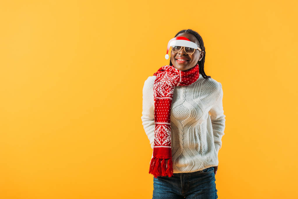 Αφρικανική Αμερικάνικη γυναίκα με χειμωνιάτικο πουλόβερ και χριστουγεννιάτικα γυαλιά απομονωμένα σε κίτρινο - Φωτογραφία, εικόνα