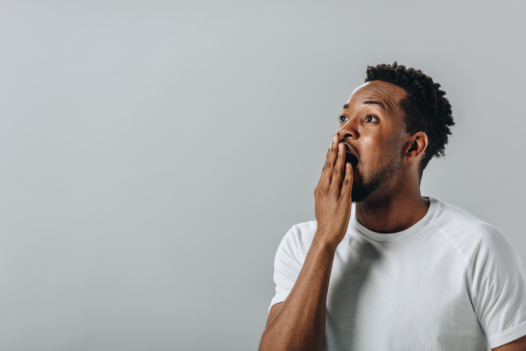 шокований афроамериканець людина в білому T-коротке покриття рот з рук і дивлячись на камеру ізольовані на сірий - Фото, зображення