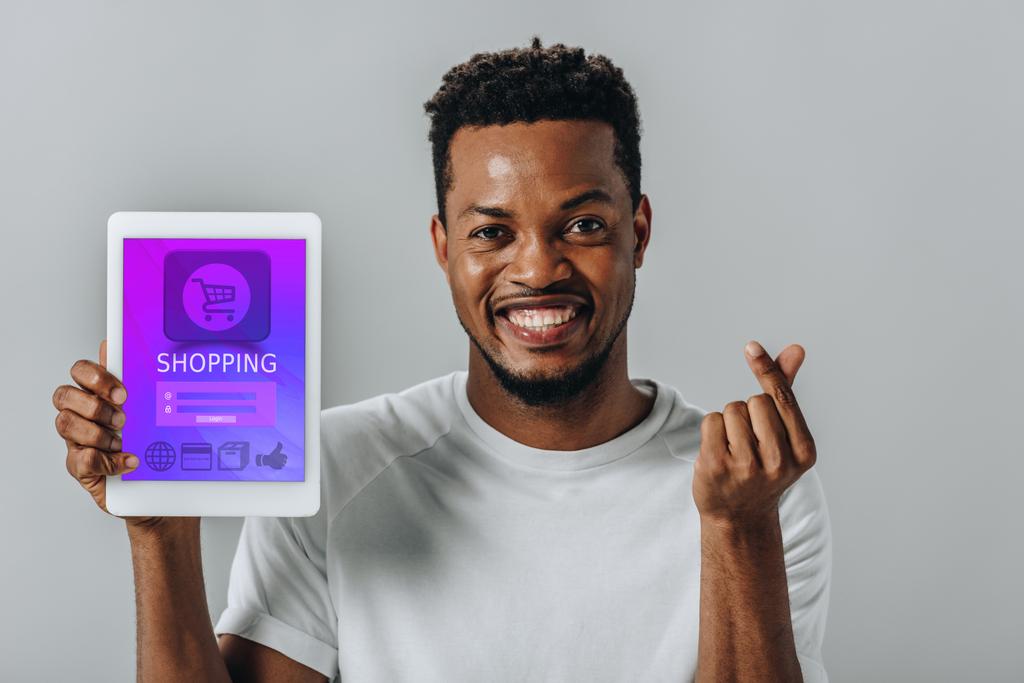 Afro-amerikai férfi gazdaság digitális tabletta vásárlási alkalmazás és pénzt mutat gesztus izolált szürke - Fotó, kép