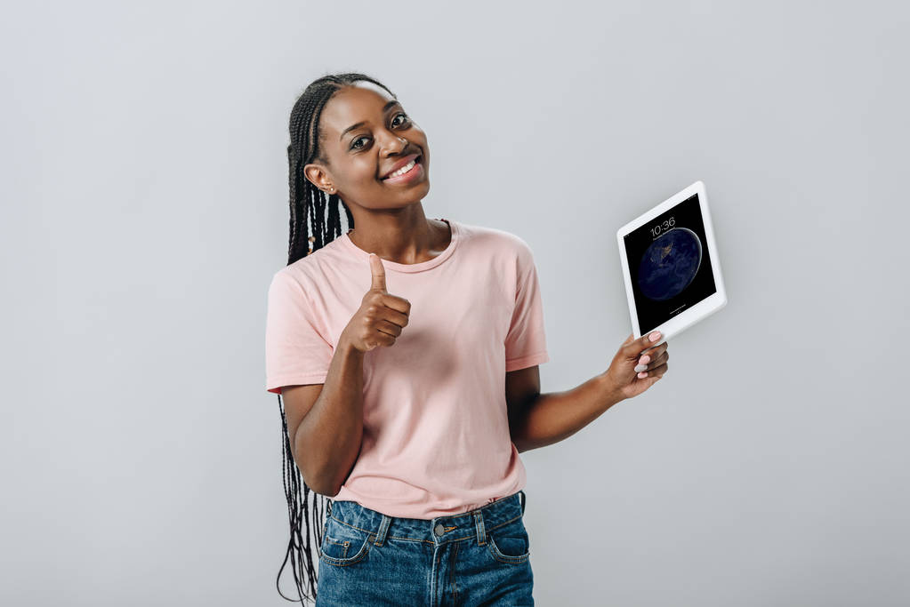 KYIV, UKRAINE AUGUST 2, 2019: Afrikkalainen amerikkalainen nainen, jolla on iPad lukitusnäytöllä ja joka näyttää peukalon eristettynä harmaalla
 - Valokuva, kuva