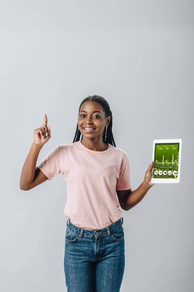 African American woman holding digital tablet with healthy lifestyle application and showing idea sign isolated on grey - Photo, Image