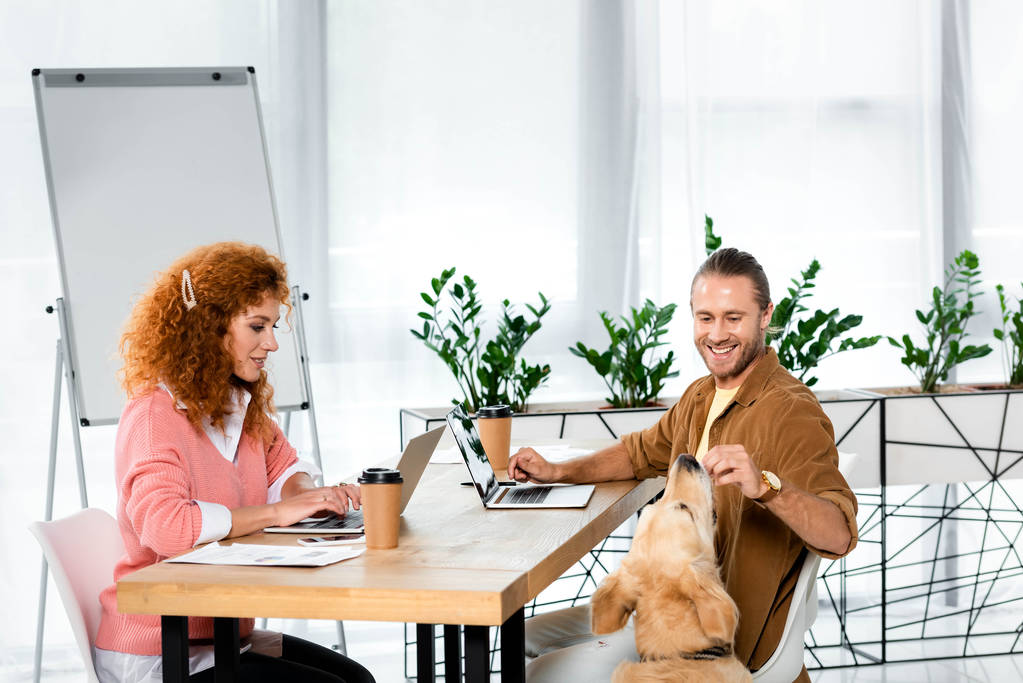 attractive woman using laptop and handsome man feeding golden retriever - Photo, Image