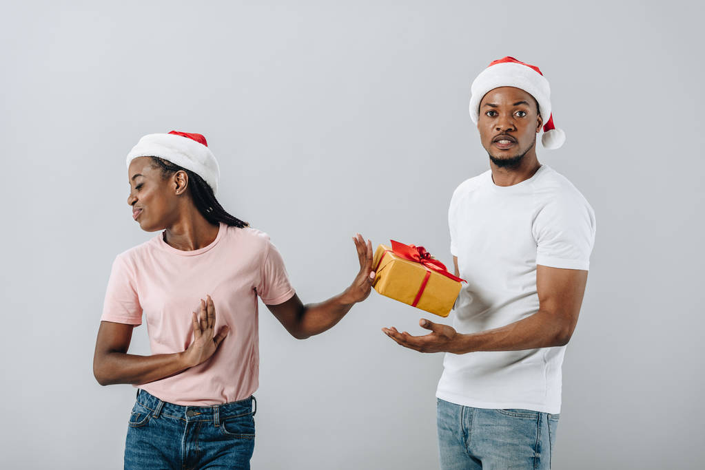 Donna afroamericana in cappello Babbo Natale respinge confezione regalo da uomo isolato su grigio
 - Foto, immagini