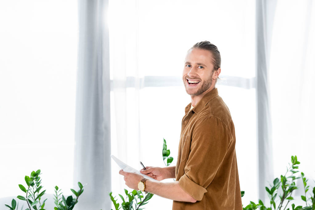 komea ja hymyilevä mies paidassa tekemässä paperitöitä toimistossa
  - Valokuva, kuva