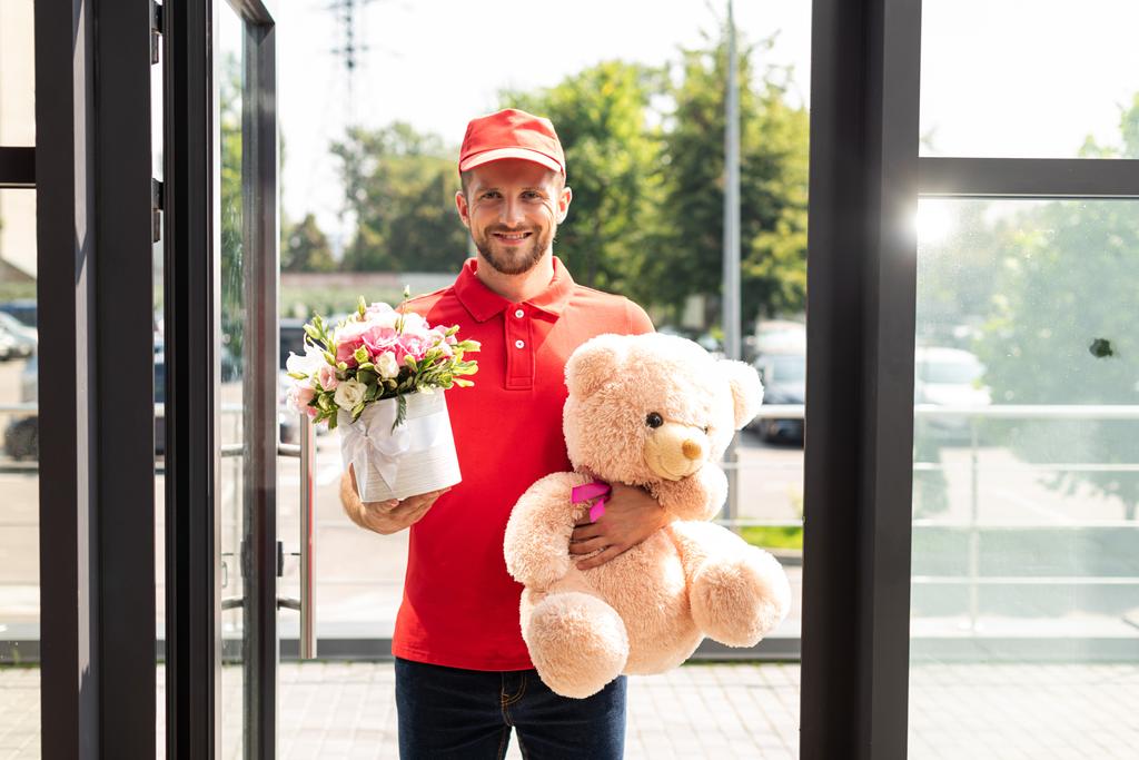 oyuncak ayı ve çiçek tutan mutlu teslimat adam  - Fotoğraf, Görsel