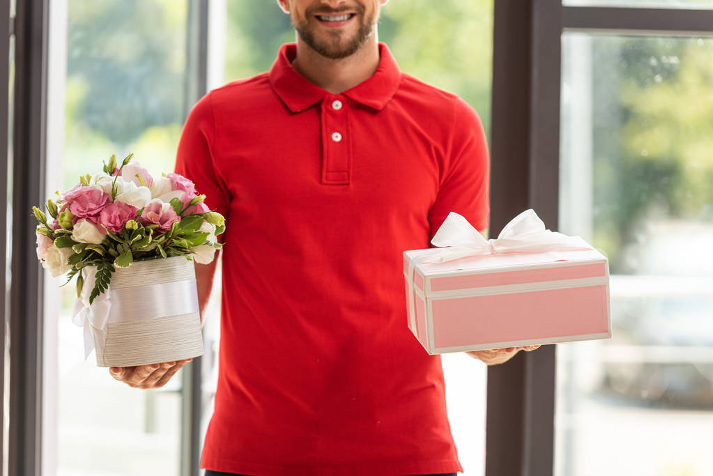 обрізаний вид веселого бородатого чоловіка, який тримає квіти та рожеву подарункову коробку
  - Фото, зображення