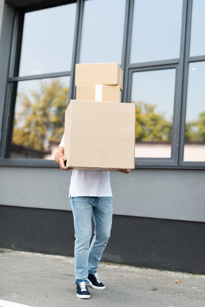 άνθρωπος παράδοσης που καλύπτει το πρόσωπο ενώ κρατώντας κουτιά κοντά στο κτίριο  - Φωτογραφία, εικόνα