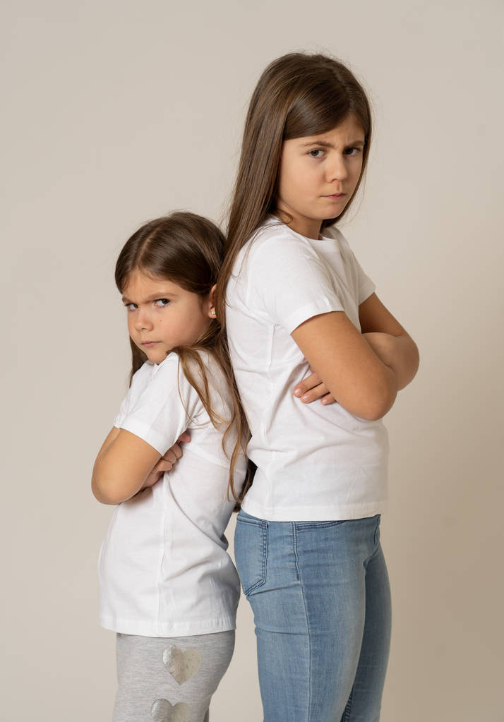 Portrait of two young siblings standing back to back not talking to each other after having an argument. Sisters not interacting angry and mad one to another in bad relationship. Studio shot. - Photo, Image