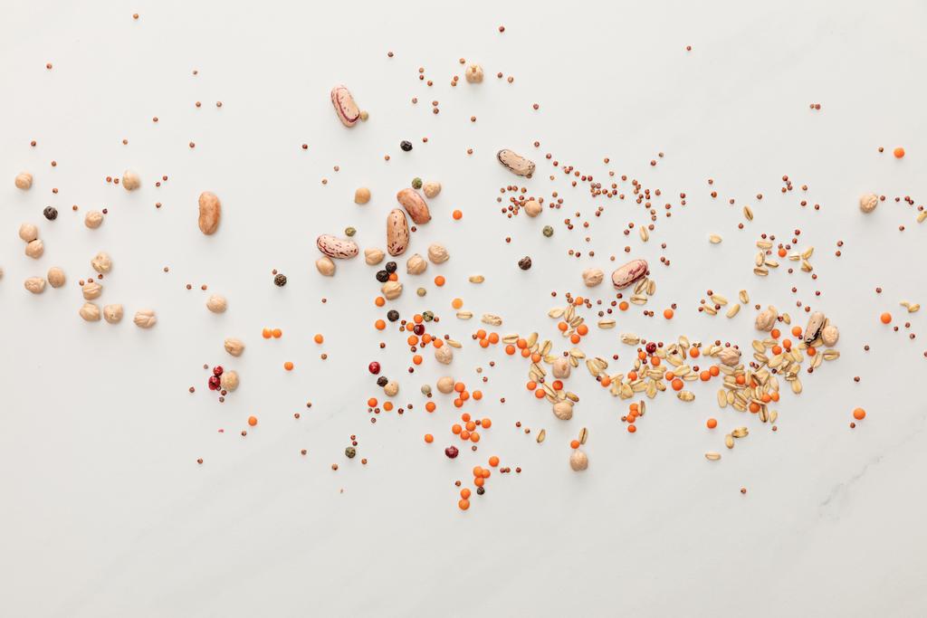 pohled na rozptýlené fazole, čočku, ovesnou stravu a peppercorny na povrchu mramoru - Fotografie, Obrázek
