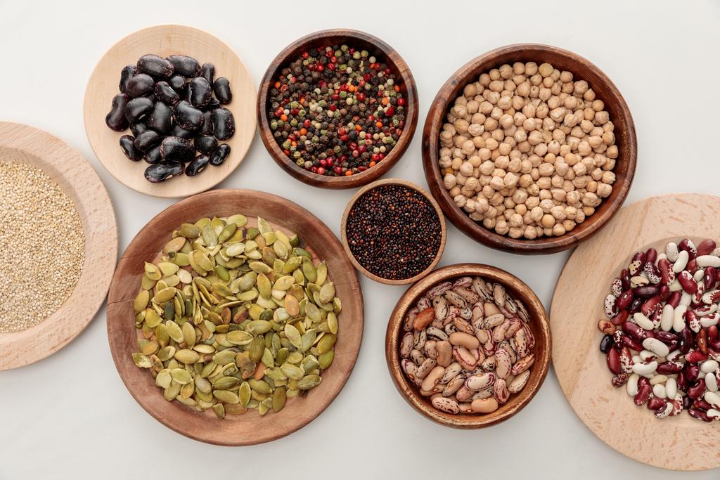 top view of wooden bowls with diverse beans, quinoa, peppercorns, pumpkin seeds and chickpea on white marble surface - Photo, Image