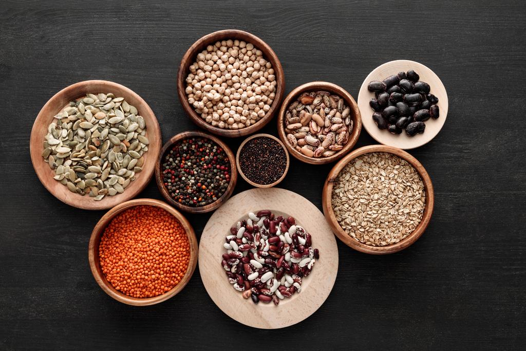 top view of various wooden plates and bowls with beans, cereals, spice and pumpkin seeds on dark wooden table - Photo, Image