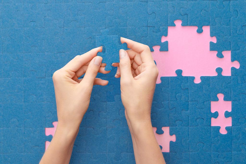 bijgesneden beeld van vrouw vasthouden van blauwe puzzel op roze achtergrond - Foto, afbeelding
