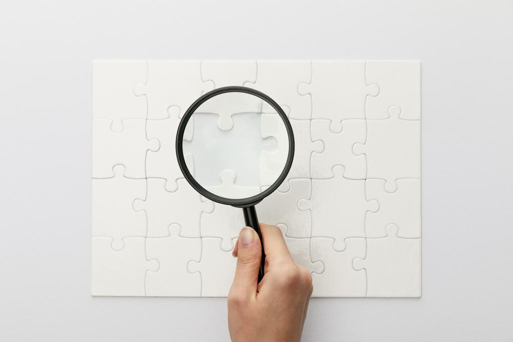 vue recadrée de la femme tenant loupe sous puzzle avec pièce perdue sur fond blanc
 - Photo, image