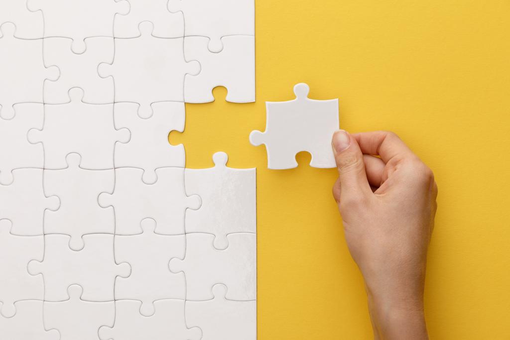 cropped view of woman putting piece of white jigsaw puzzle on yellow background - Photo, Image