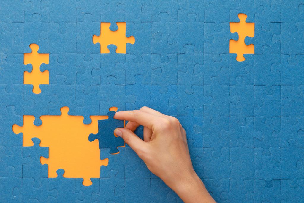 cropped view of woman putting piece of blue jigsaw puzzle on yellow background - Photo, Image