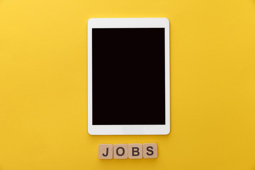 felülnézet a digitális tabletta, üres képernyő és karton négyzetek munkahelyek felirattal a sárga háttér - Fotó, kép