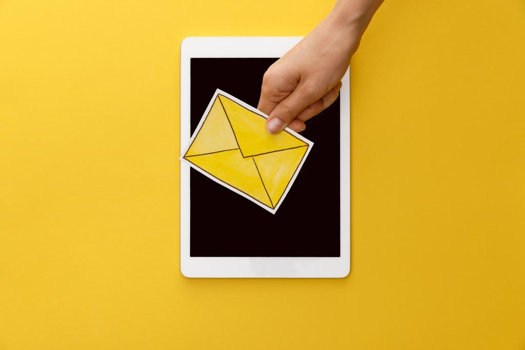 обрізаний вид жінки, що тримає лист під цифровим планшетом з порожнім екраном на жовтому фоні
 - Фото, зображення