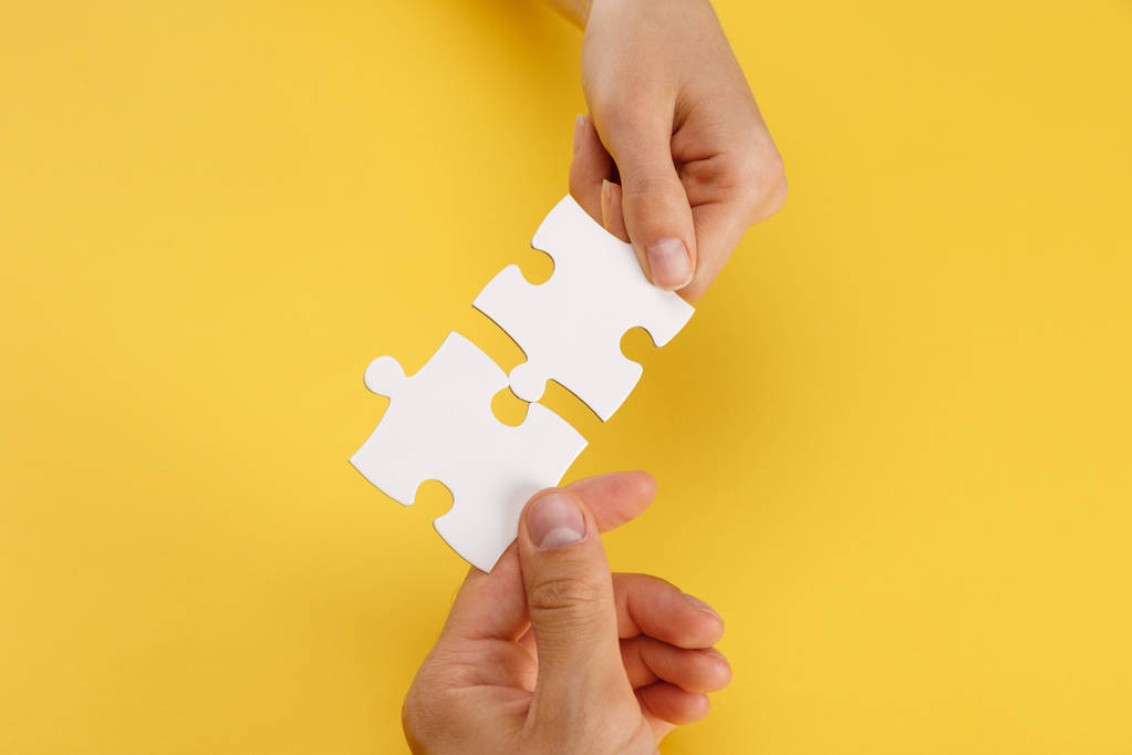 cropped view of woman and man matching pieces of white puzzle on yellow background - Photo, Image