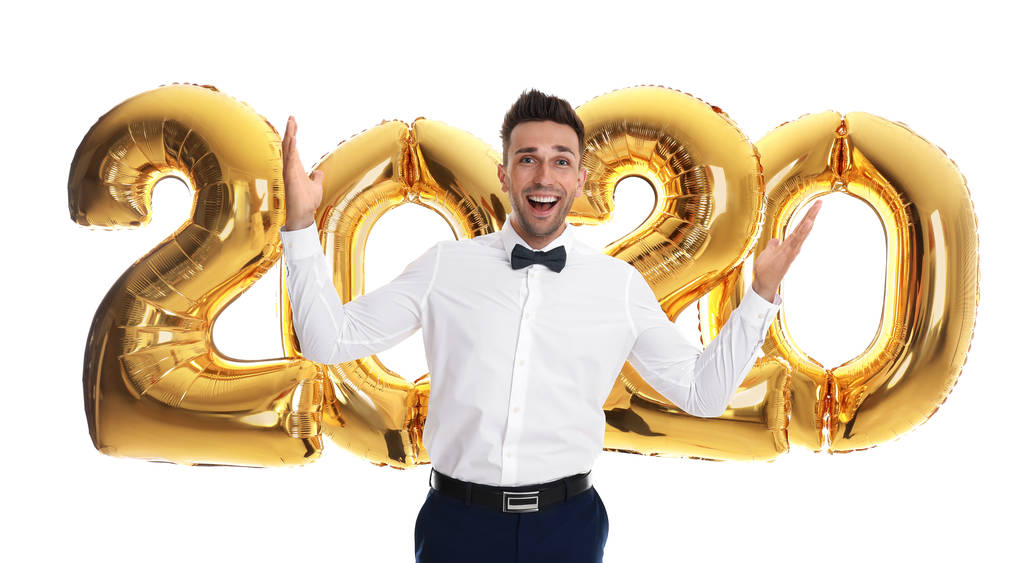 Ευτυχισμένο νεαρό άντρα κοντά σε χρυσά μπαλόνια 2020 σε λευκό φόντο. Εορτασμός της Πρωτοχρονιάς - Φωτογραφία, εικόνα